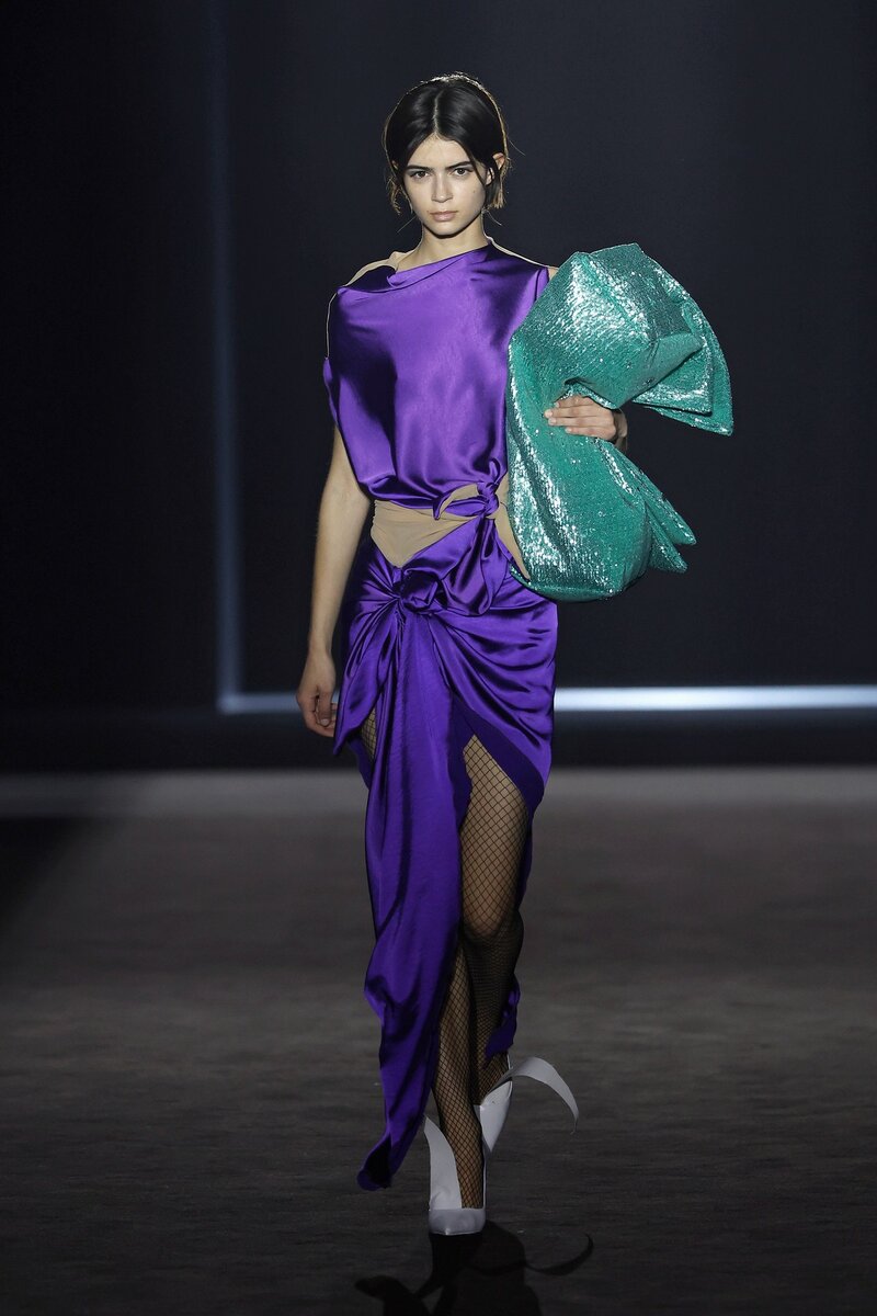 Model parading at 080 Barcelona Fashion in an Ernesto Nara look consisting of a two-piece dress with a violet bow at the waist and an aqua green maxi bag