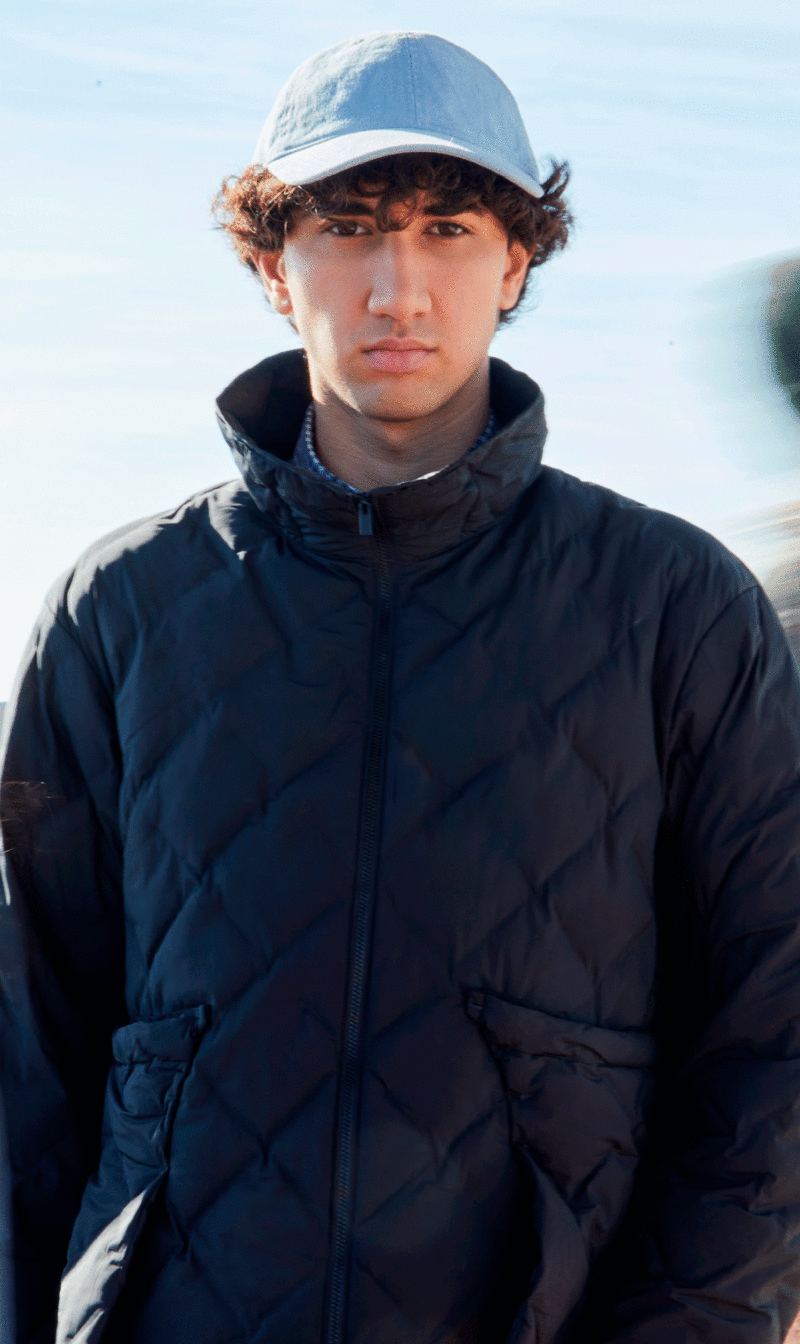 A boy wearing a cap and a dark blue unisex quilted jacket
