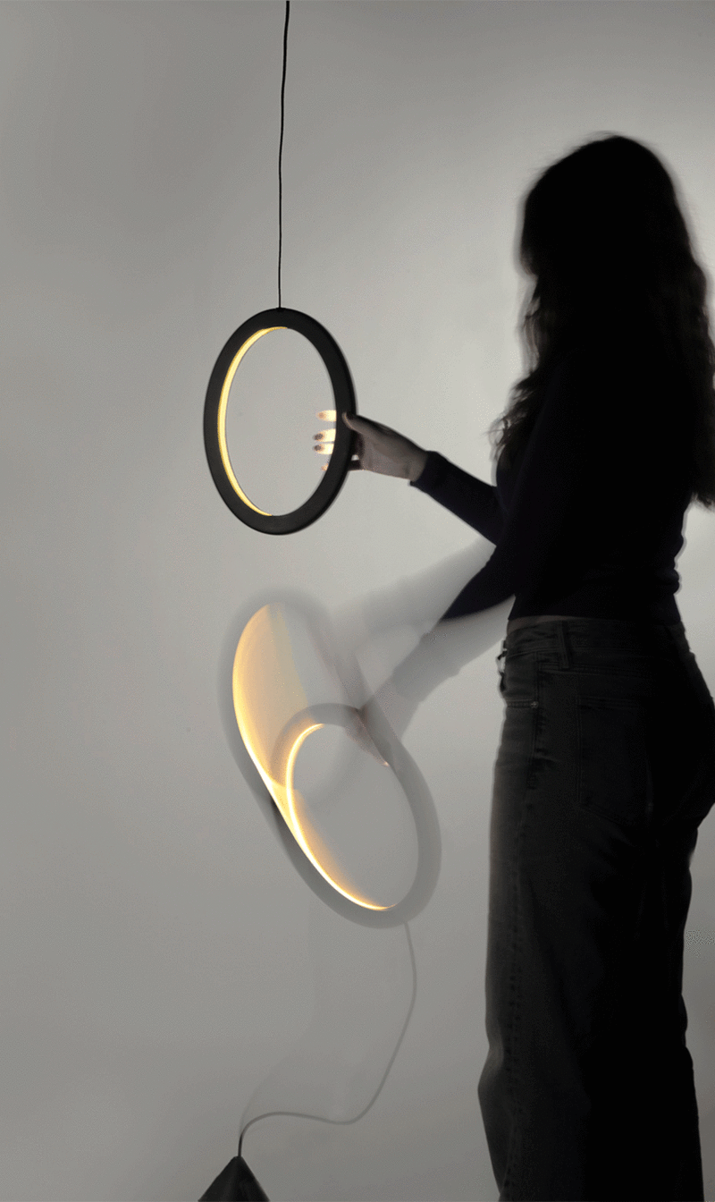 Young woman with his back turned holding a hanging lamp made up of two large separable rings joined together by magnets