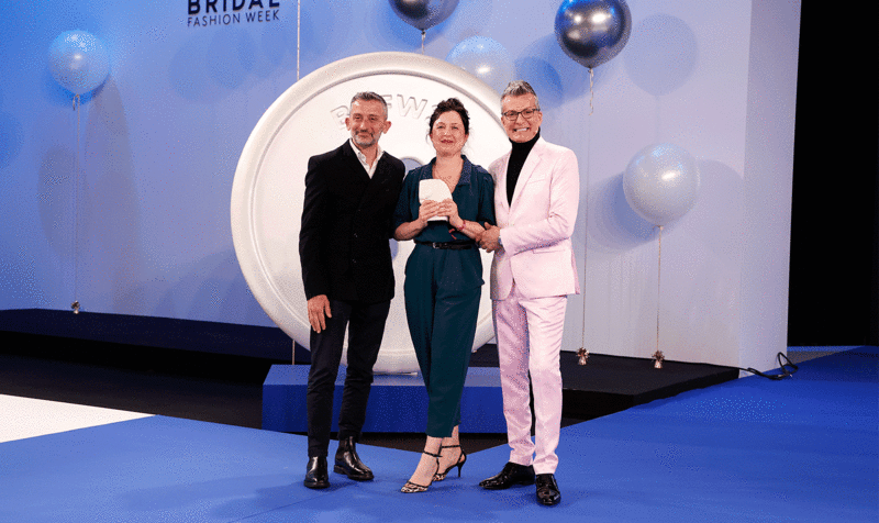 Photo of the Barcelona Bridal & Fashion Awards with Andrea Marchesi on the left, next to the award-winning designer and the gala host in front of a blue background.