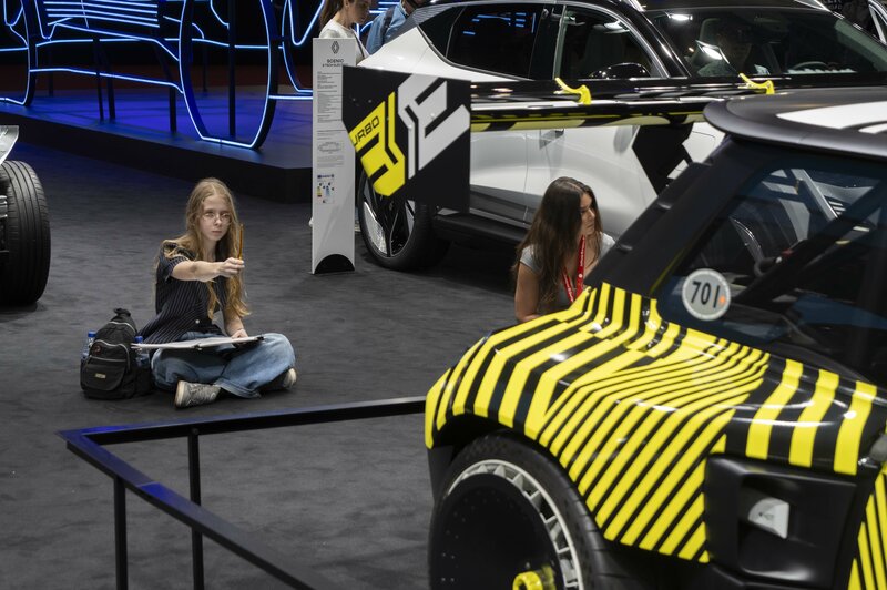 A student sitting on the floor sketching a yellow and black car in the foreground