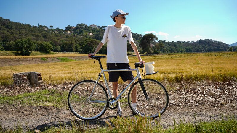A cyclist in the countryside on a sunny day. The bike has a white cylindrical device hanging from the handlebars.