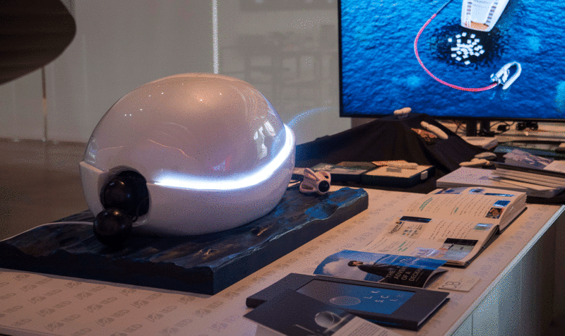 Display table with a screen in the background on the right and elements arranged on it, including a white shell-shaped robot.