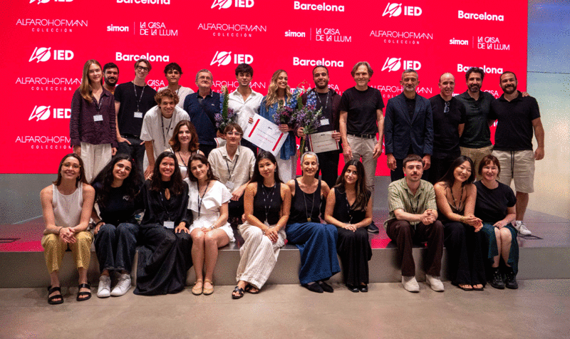 Twenty people on stage posing for a group photo with a red screen in the background with the IED Barcelona logo.