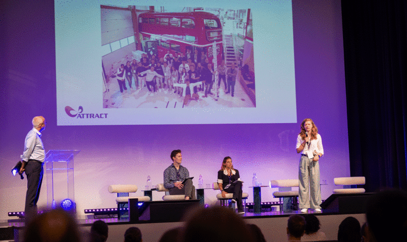 Conference setting with four people, two seated and two standing, addressing the audience