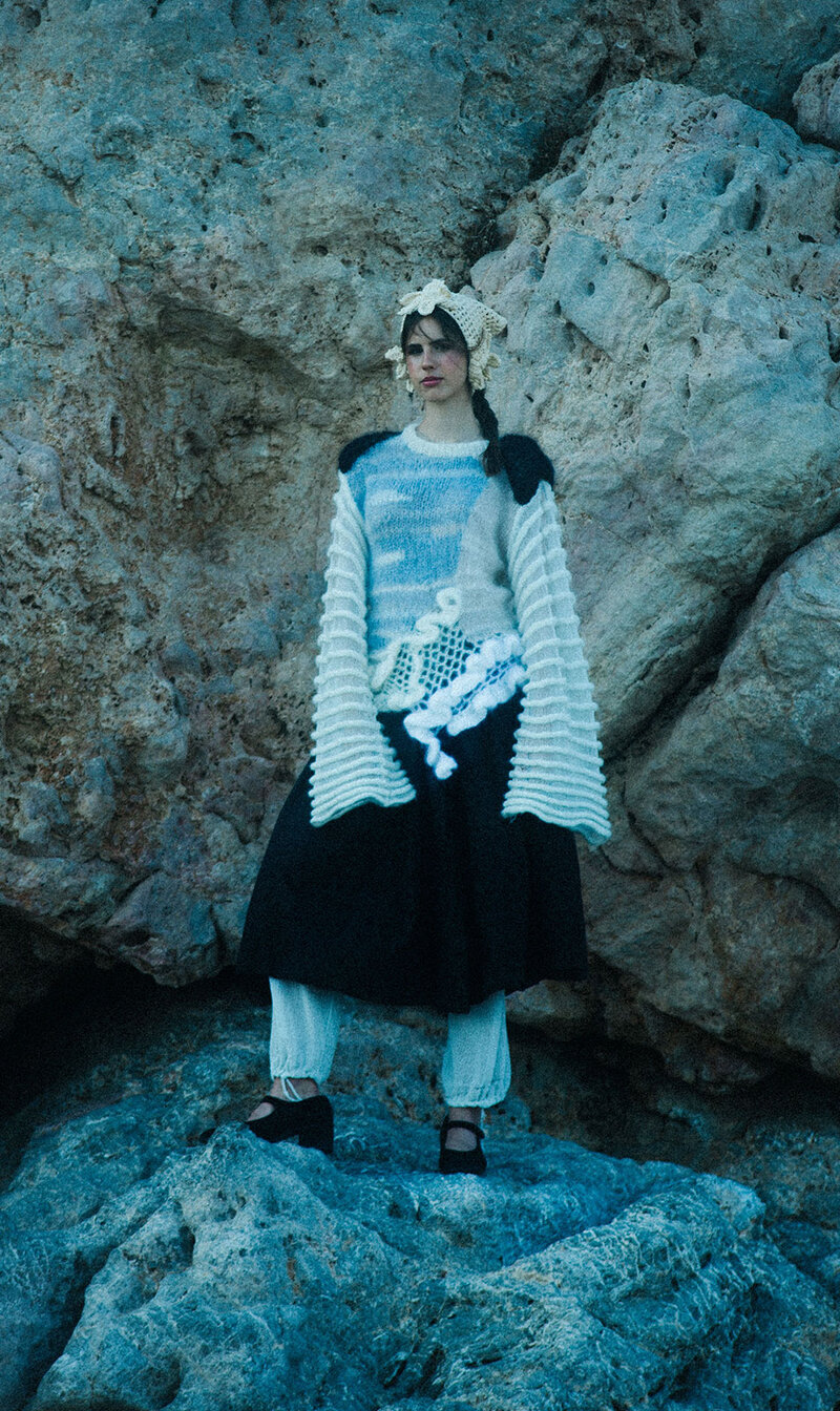 Young model standing on a rock with a wide-sleeved sweater hanging off