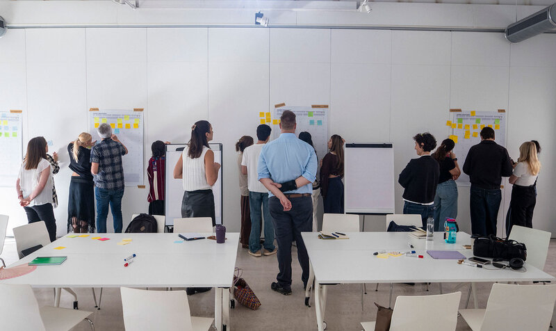 A university classroom with people writing in groups on several whiteboards