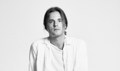 Close-up of a man in a shirt and with light hair looking at the camera. Black and white photo.