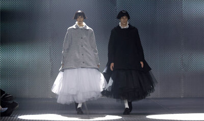 Two models, each wearing a voluminous skirt, walk down a catwalk