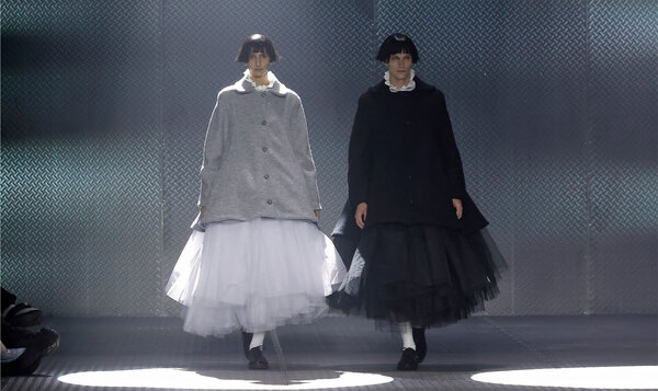 Two models, each wearing a voluminous skirt, walk down a catwalk