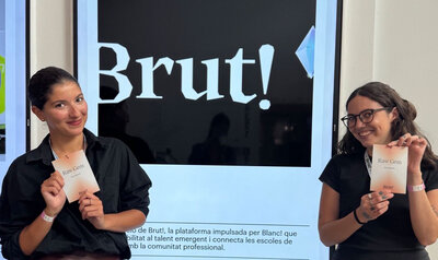 Two girls holding a paper program in front of a design festival poster