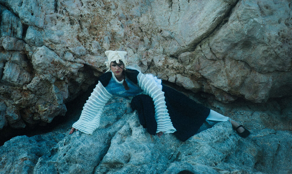 Female model posing on a rock wearing a white wool wide-sleeved sweater