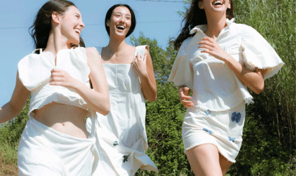 Three girls dressed in white running in a garden on a sunny day