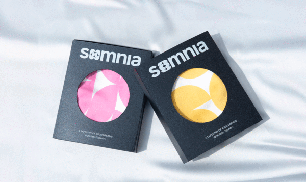 Two black boxes with a central hole where you can see a fabric with colored patterns and the word SOMNIA on the packaging.